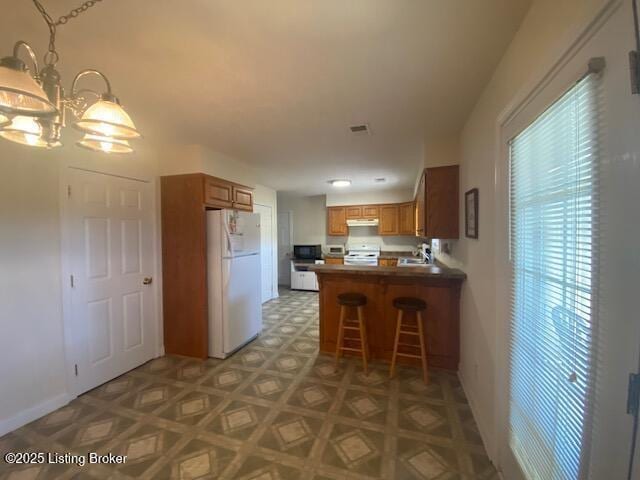 kitchen featuring brown cabinets, freestanding refrigerator, a chandelier, black microwave, and a peninsula