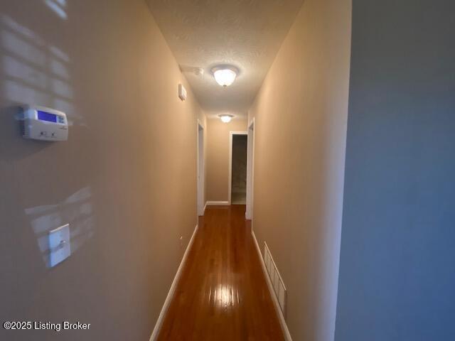 hallway featuring a textured ceiling, wood finished floors, visible vents, and baseboards