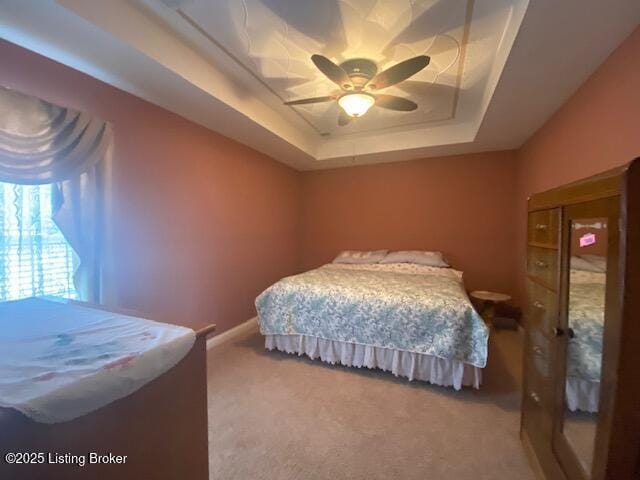 bedroom with ceiling fan, baseboards, a raised ceiling, and carpet flooring