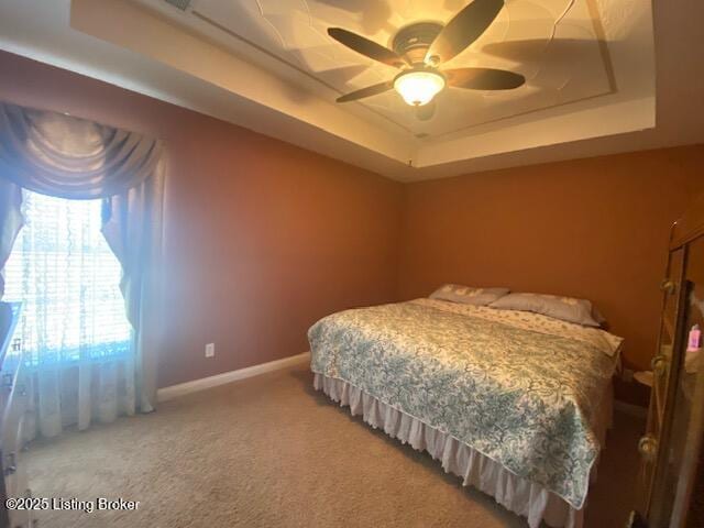 carpeted bedroom featuring a ceiling fan, a raised ceiling, and baseboards