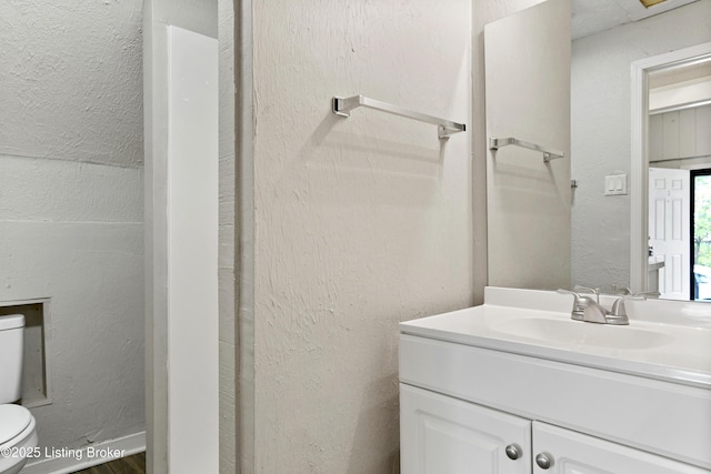 bathroom featuring toilet, vanity, and a textured wall