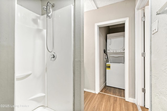 bathroom featuring walk in shower, wood finished floors, and stacked washer and clothes dryer