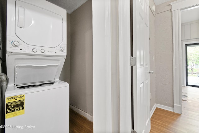 laundry area with a textured wall, laundry area, wood finished floors, baseboards, and stacked washer and clothes dryer