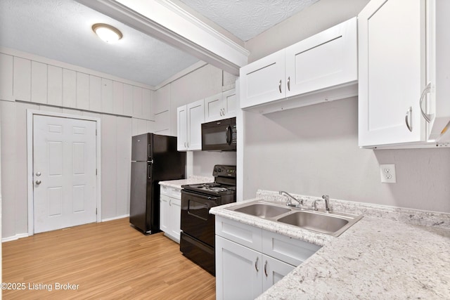 kitchen featuring a textured ceiling, light wood-type flooring, black appliances, white cabinetry, and a sink