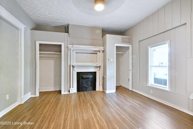 unfurnished living room with a textured ceiling, a fireplace, wood finished floors, visible vents, and baseboards