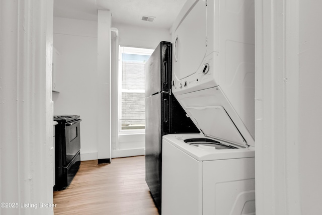 clothes washing area featuring stacked washer and dryer, plenty of natural light, visible vents, and light wood-style floors