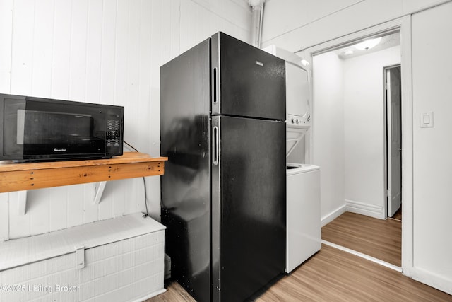 kitchen featuring black appliances, wood finished floors, stacked washer and clothes dryer, and baseboards