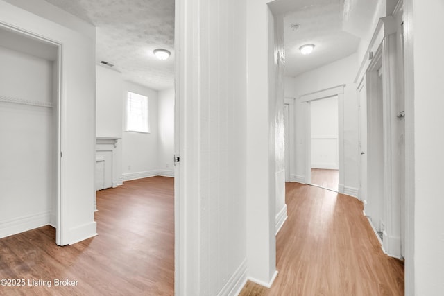 hallway featuring a textured ceiling, light wood finished floors, visible vents, and baseboards