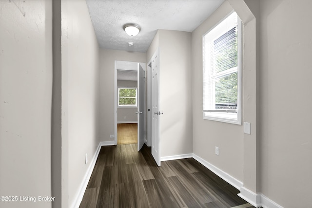 corridor featuring baseboards, dark wood finished floors, and a textured ceiling