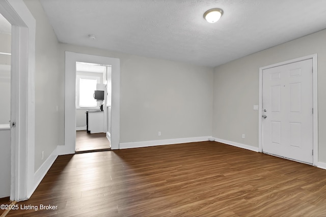 unfurnished room with a textured ceiling, baseboards, and wood finished floors