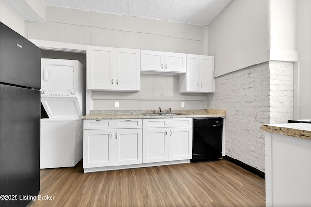 kitchen featuring black appliances, stacked washer / dryer, a sink, and white cabinetry