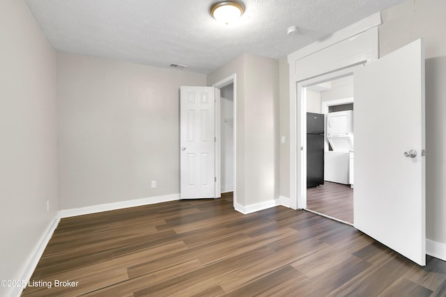 unfurnished bedroom with a textured ceiling, visible vents, baseboards, freestanding refrigerator, and dark wood finished floors