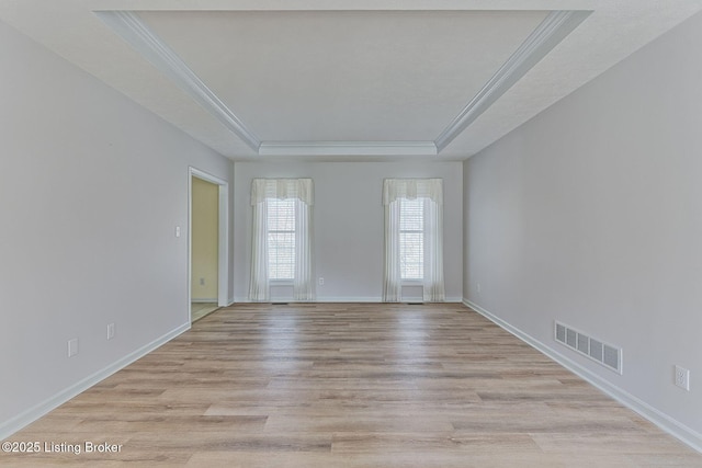 spare room featuring visible vents, baseboards, light wood-style floors, ornamental molding, and a tray ceiling