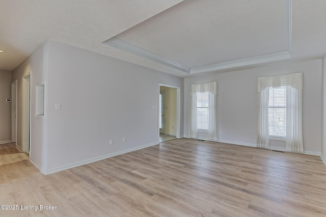 spare room with light wood-style flooring, visible vents, a tray ceiling, and baseboards