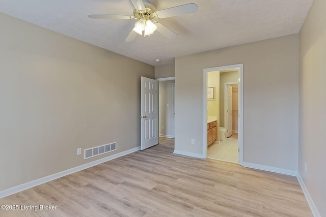 unfurnished bedroom featuring a textured ceiling, ensuite bathroom, visible vents, baseboards, and light wood-style floors