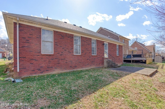 rear view of house with a deck, a lawn, and brick siding