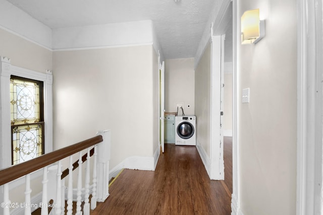 hallway with washer / dryer, baseboards, wood finished floors, a textured ceiling, and an upstairs landing