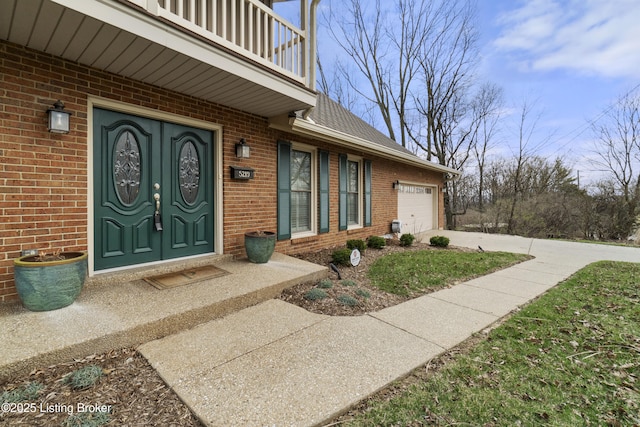 view of exterior entry with a garage, driveway, brick siding, and a balcony