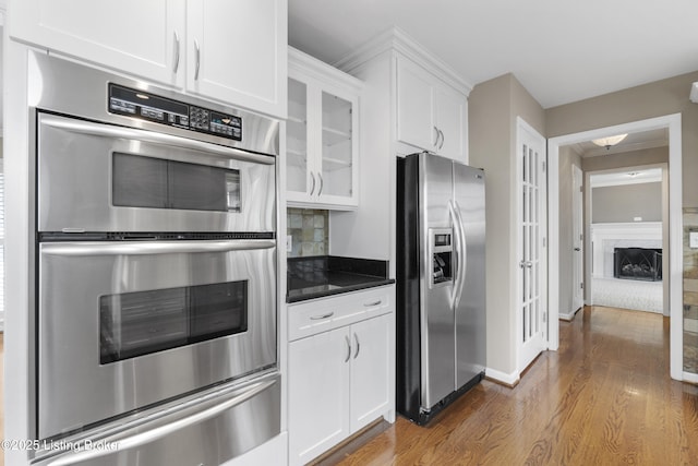 kitchen featuring dark countertops, wood finished floors, stainless steel appliances, white cabinets, and glass insert cabinets