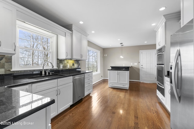 kitchen with dark wood-style floors, a sink, decorative backsplash, stainless steel appliances, and white cabinetry