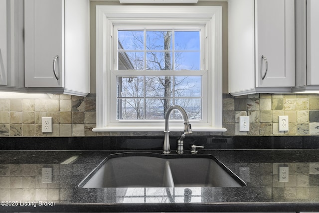 kitchen featuring dark stone countertops, decorative backsplash, white cabinets, and a sink