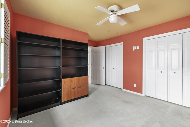 unfurnished bedroom with carpet flooring, ceiling fan, baseboards, and multiple closets