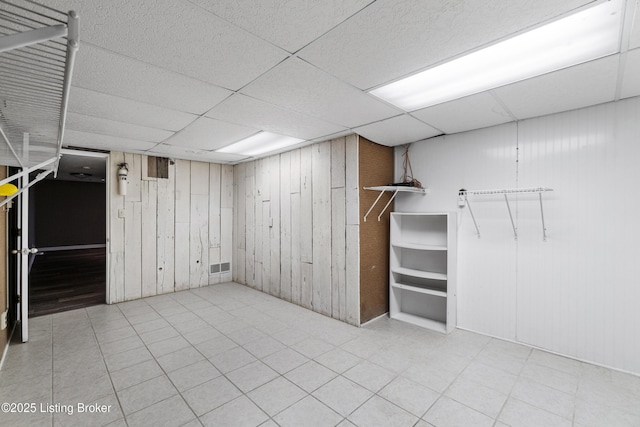 finished basement with wooden walls, visible vents, and a drop ceiling