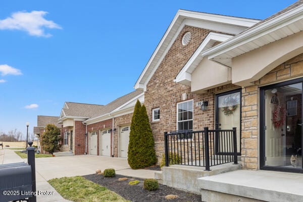 entrance to property with concrete driveway, brick siding, an attached garage, and stone siding