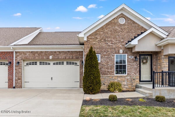 view of front of home with driveway, a shingled roof, stone siding, an attached garage, and brick siding