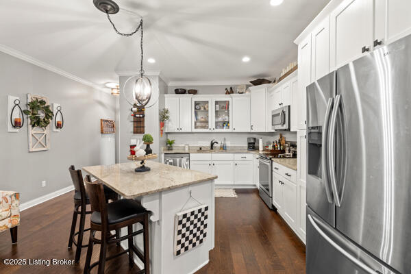 kitchen featuring appliances with stainless steel finishes, ornamental molding, white cabinetry, a kitchen island, and a kitchen bar