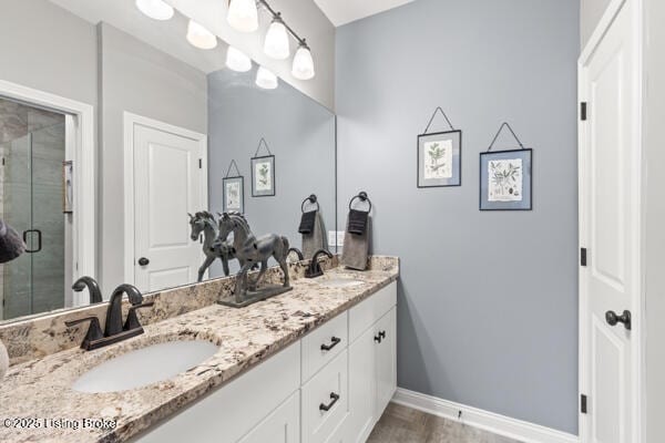 full bath featuring a shower stall, double vanity, a sink, and baseboards