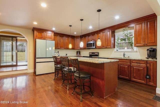 kitchen with stainless steel appliances, a kitchen breakfast bar, hanging light fixtures, a center island, and dark wood-style floors