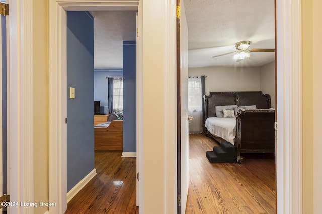 bedroom with wood-type flooring, a textured ceiling, baseboards, and a ceiling fan