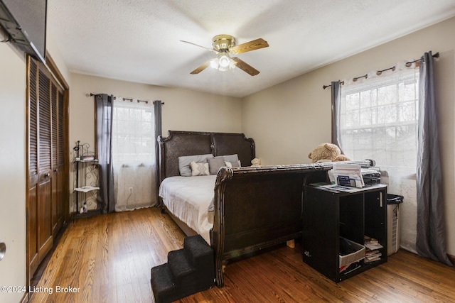 bedroom with a closet, multiple windows, wood finished floors, and a ceiling fan