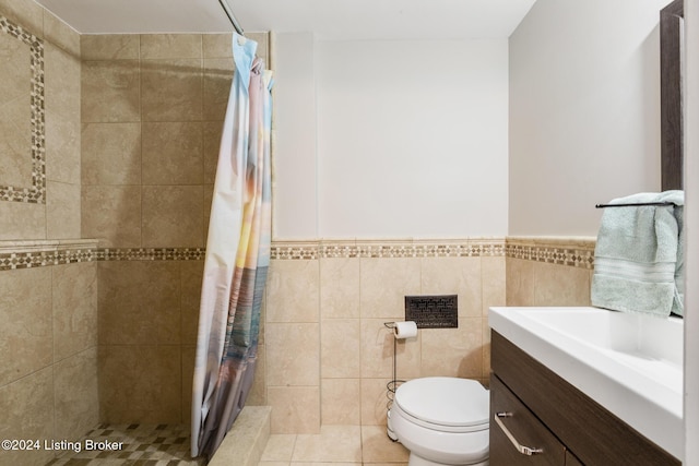 bathroom featuring toilet, vanity, tile walls, tiled shower, and wainscoting