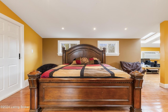 bedroom with light wood finished floors, multiple windows, baseboards, and a wall mounted AC