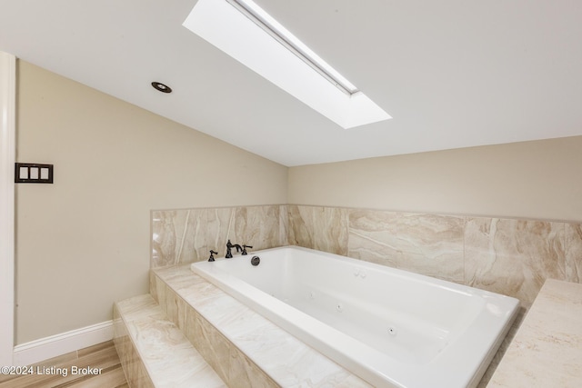 full bath with a whirlpool tub, vaulted ceiling with skylight, baseboards, and wood finished floors