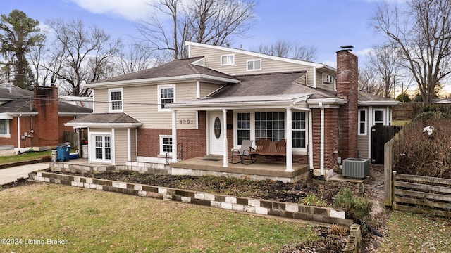 back of property with central AC unit, a lawn, a chimney, a porch, and brick siding