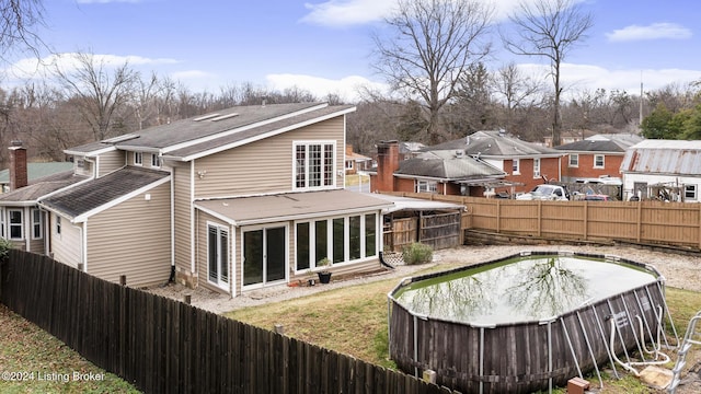 back of property featuring a covered pool, a fenced backyard, and roof with shingles