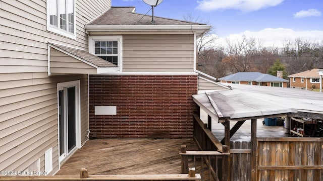 view of side of home featuring a deck, a shingled roof, and brick siding