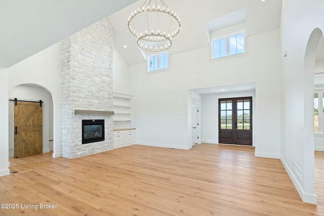 unfurnished living room with visible vents, light wood finished floors, a fireplace, a barn door, and a notable chandelier