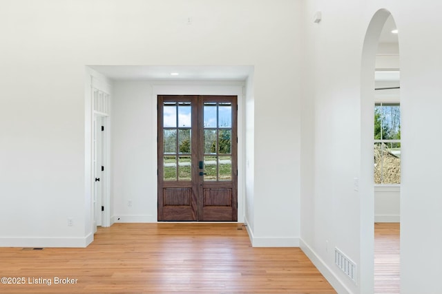 entryway featuring visible vents, french doors, arched walkways, light wood-style floors, and baseboards