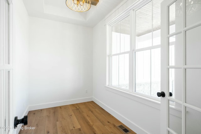 unfurnished room featuring visible vents, a raised ceiling, light wood-style floors, baseboards, and a chandelier