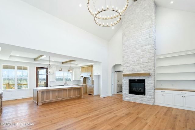 unfurnished living room featuring arched walkways, light wood-style floors, a fireplace, baseboards, and a chandelier