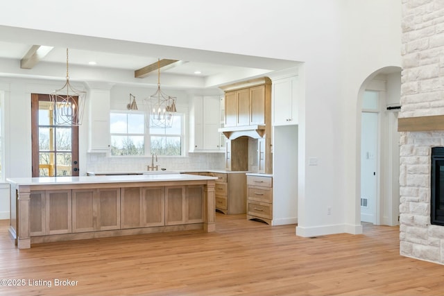 kitchen featuring beam ceiling, a stone fireplace, light wood-style floors, a notable chandelier, and a center island