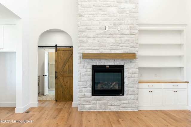 unfurnished living room featuring a barn door, baseboards, light wood-style floors, and built in shelves