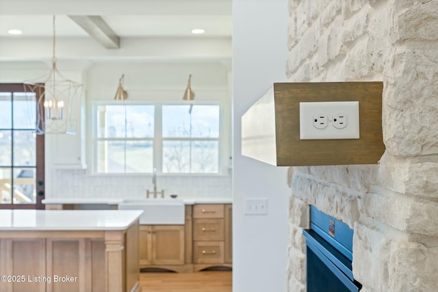 kitchen featuring beam ceiling, a notable chandelier, a sink, a fireplace, and light countertops