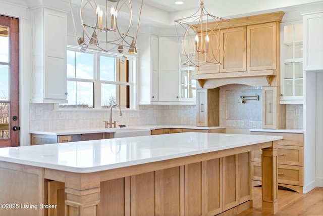 kitchen with a notable chandelier, a sink, backsplash, light countertops, and glass insert cabinets