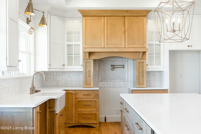 kitchen featuring light wood-type flooring, an inviting chandelier, a sink, glass insert cabinets, and tasteful backsplash