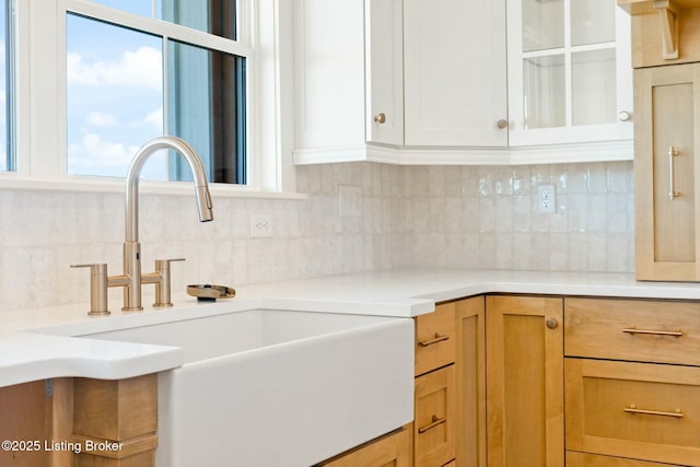 kitchen featuring tasteful backsplash, light countertops, glass insert cabinets, and a sink